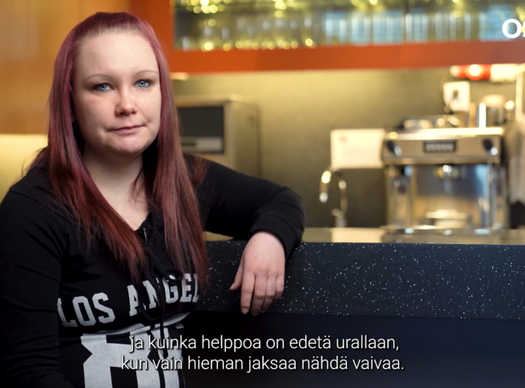 Nuori nainen nojaa pöytään. Taustalla keittiötarvikkeita.