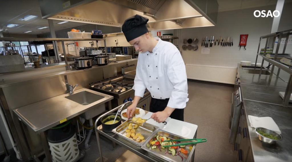 Kokin työvaatteisiin pukeutunut henkilö ravintolan keittiössä.