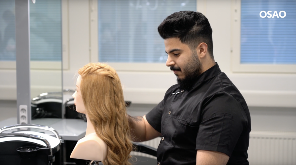 Parturi-kampaajaopiskelija Mohammed harjaa alan harjoituspään hiuksia.