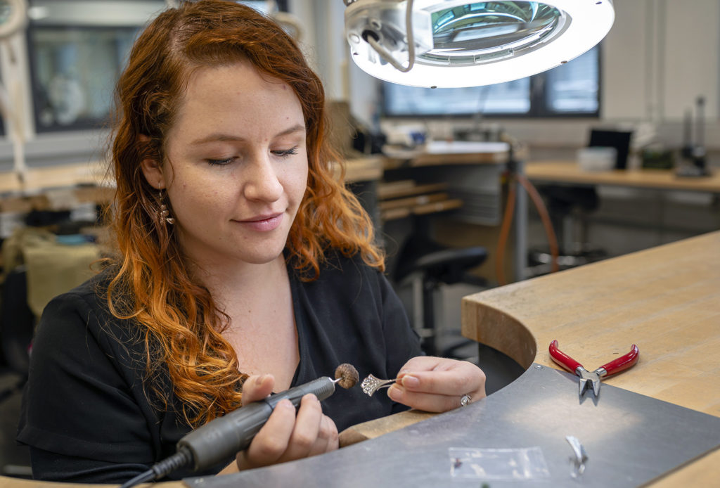 Punahiuksinen nainen valmistaa pöydän ääressä korua.