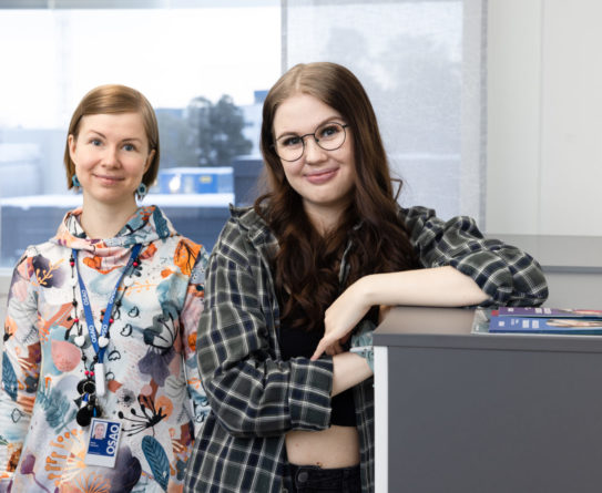 Opiskelija Oona Kinanen ja opinto-ohjaaja Maria Nykänen seisovat vierekkäin. Oona nojaa käsivarttaan hyllykköön..