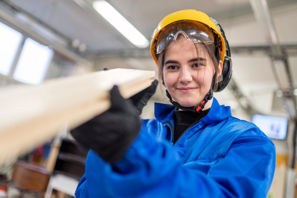 Sahaprosessinhoitaja työskentelee sinisessä haalarissa ja tarkkailee laudan suoruutta.