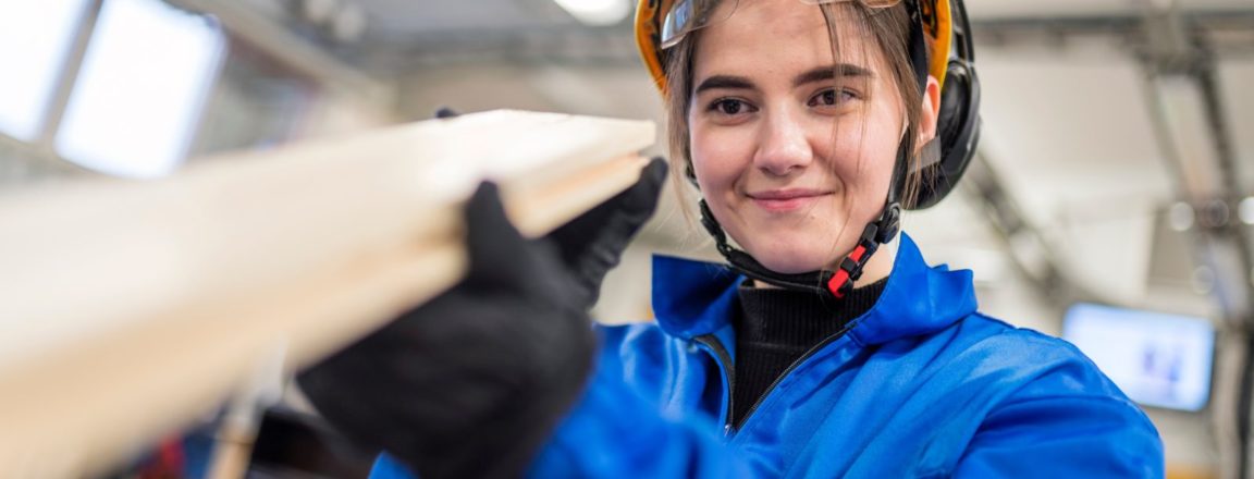 Sahaprosessinhoitaja työskentelee sinisessä haalarissa ja tarkkailee laudan suoruutta.