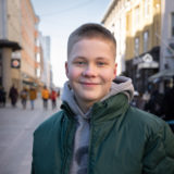 Nuori mies vihreässä takissa seisoo Oulun keskustassa.