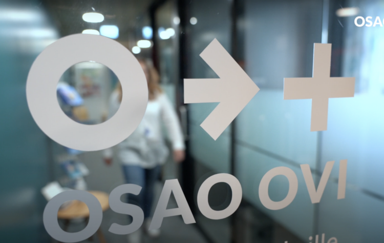 Lasiovi, jossa on iso o-kirjain, nuoli ja plusmerkki sekä alla teksti OSAO Ovi. Oven toisella puolella lähestyy valkopaitainen henkilö ovea.