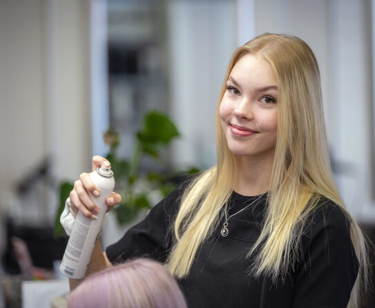 Sonja Kemppainen suihkuttaa hiuslakkaa asiakkaan hiuksiin.