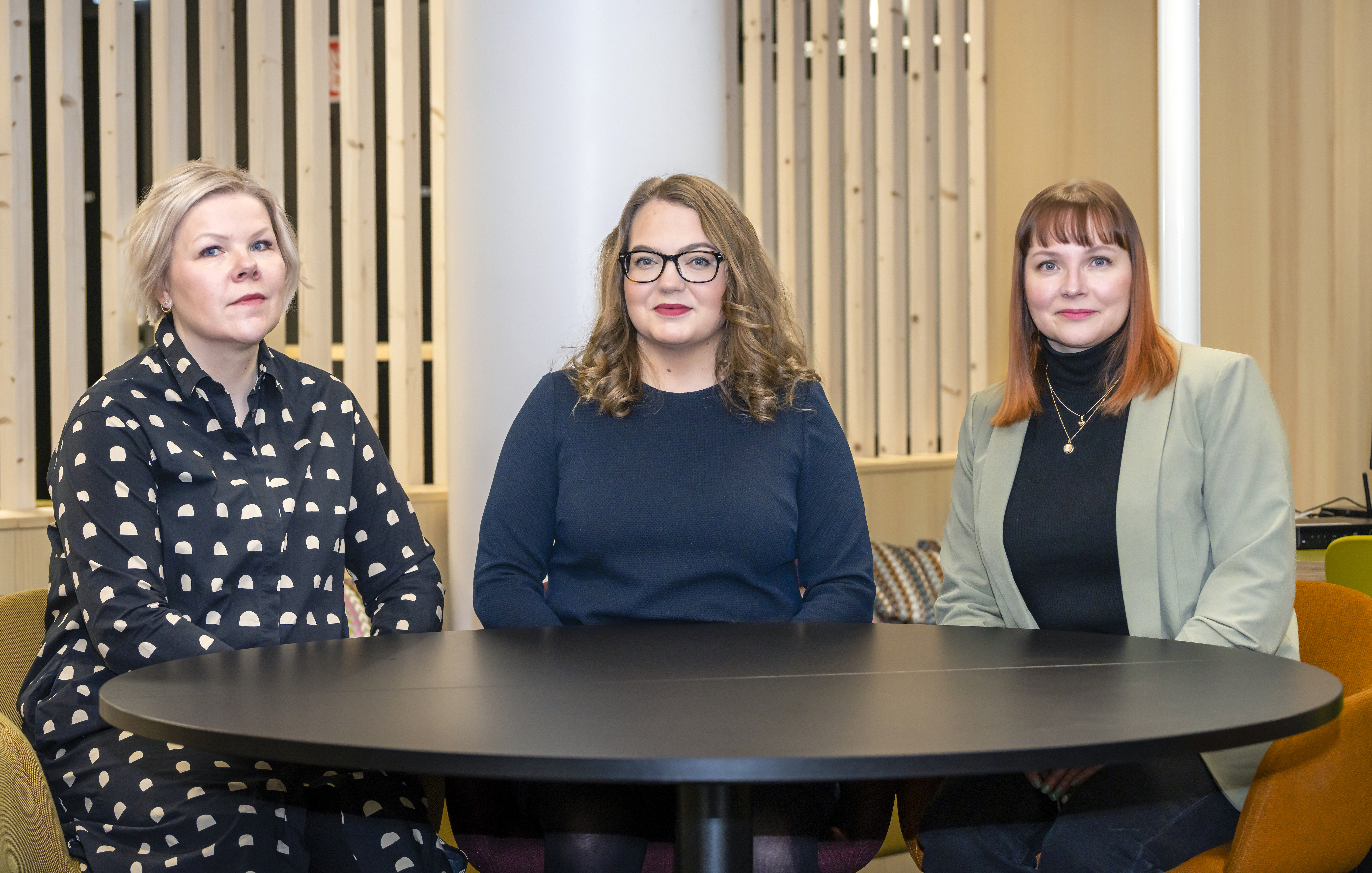Kuvassa Tiina Niemelä, Anni Karinkanta ja Heli Laitila istumassa mustan pyöreän pöydän ympärillä.