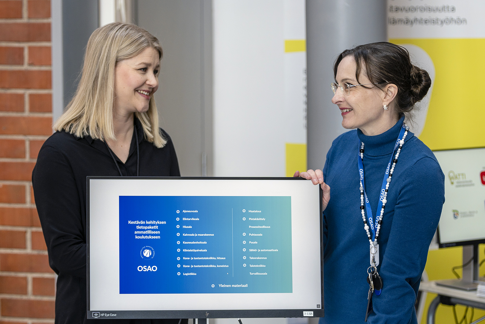 Mirja Hietala kuvassa oikealla ja Elina Halkola kuvassa vasemmalla. He seisovat tietokoneruudun edessä, jolla näkyy esitys otsikolla Kestävän kehityksen tietopaketit ammatilliseen koulutukseen. 