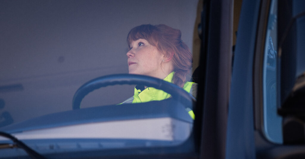 Nainen keltaisissa työvaatteissa ajaa kuorma-autoa.