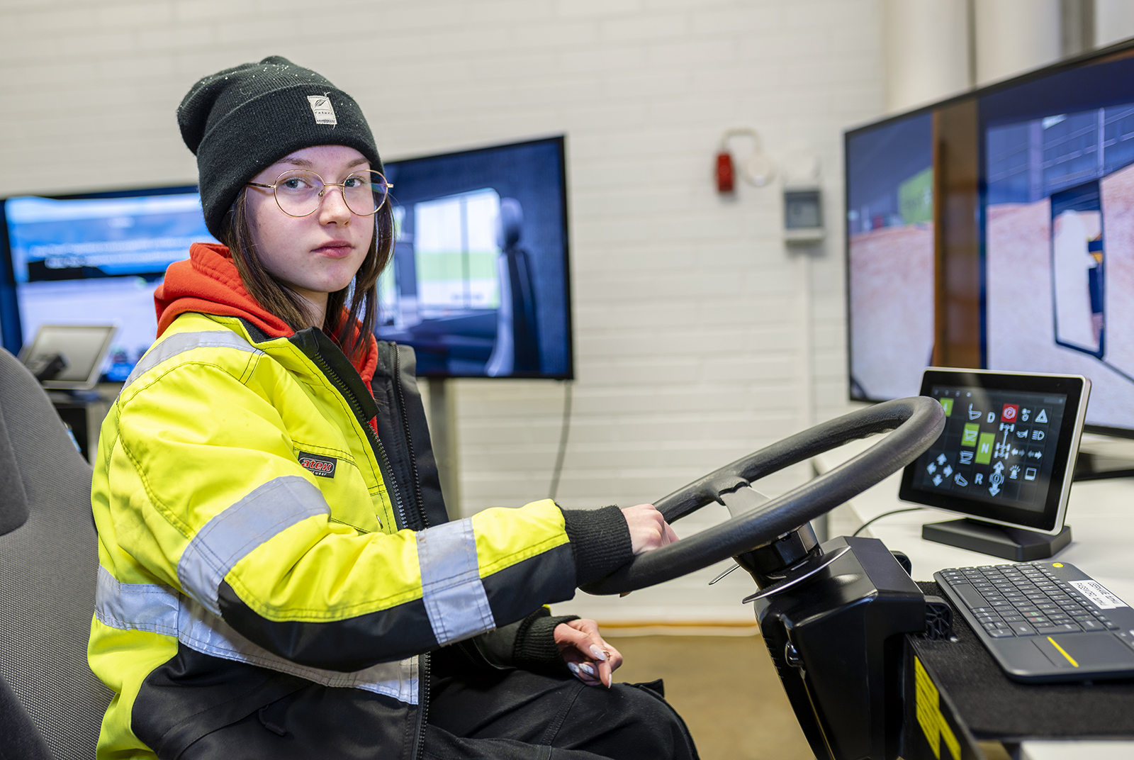 Jenna Puhakka kuvattuna ajoneuvosimulaattorin ratissa päällään keltainen huomiotakki.