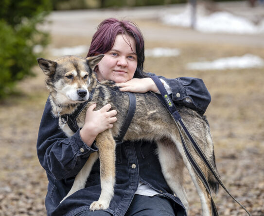 Mirella Puruunen kuvattuna luonnossa valko-harmaan Hilla-koiran kanssa.