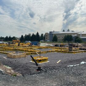 Rakennustyömaa-alue, jossa on valutyöt käynnissä. Taustalla näkyy puistoa ja keltainen iso tiilirakennus.