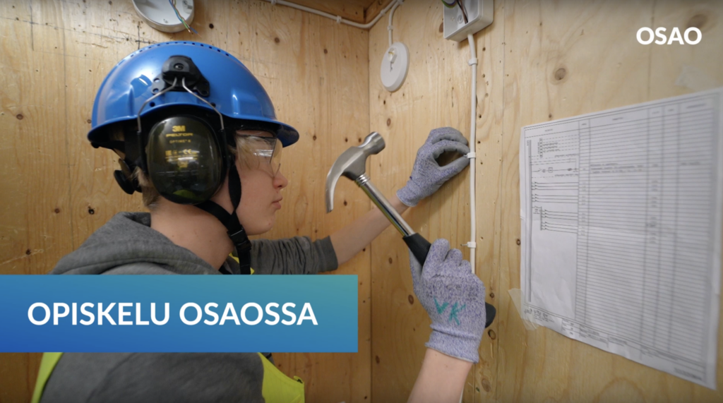 Henkilö naulaa vasaralla kiinnikettä seinään.