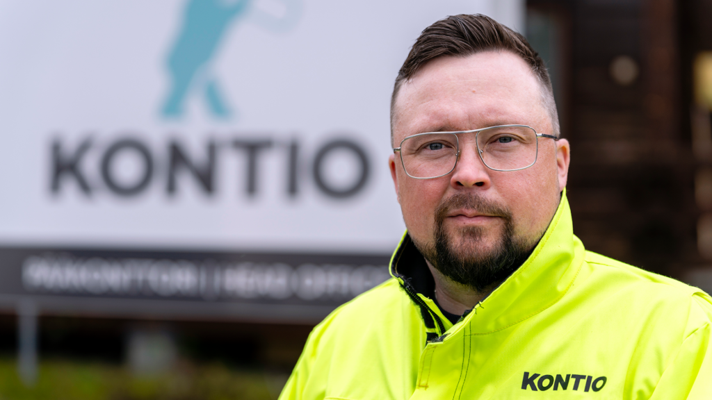 Mies keltaisessa takissa seisoo ulkona, taustalla näkyy Kontio-yrityksen kyltti.