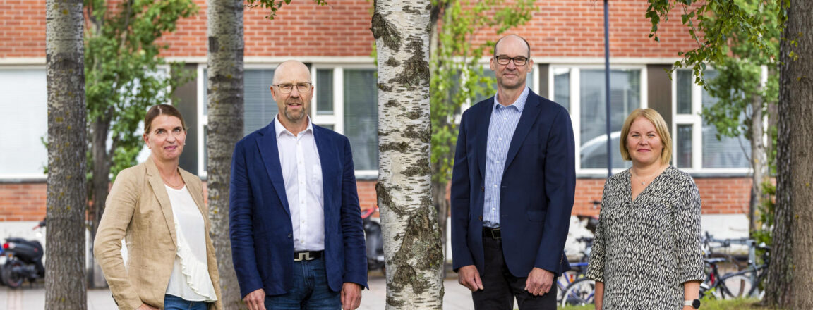 Neljä johtajaa seisovat koiuvn alla ja katsovat kameraan.