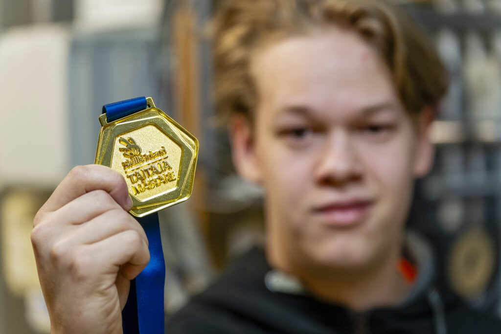 Henkilö pitää kädessään kultaista mitalia, jossa lukee 'Taitaja'.