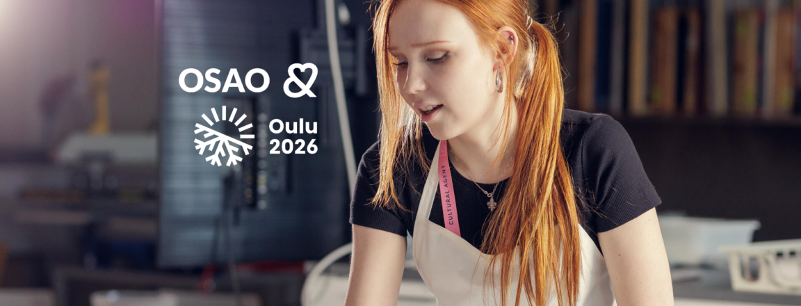 Nuori nainen seisoo tekstiilialan luokassa päällään esiliina ja kaulassa kaulanauha, jossa lukee Cultural Agent. Hänen vieressään on OSAO ja Oulu2026 logot. Hänellä on pitkät punaiset hiukset ja hän katsoo alaspäin keskittyneenä johonkin edessään olevassa työssä.