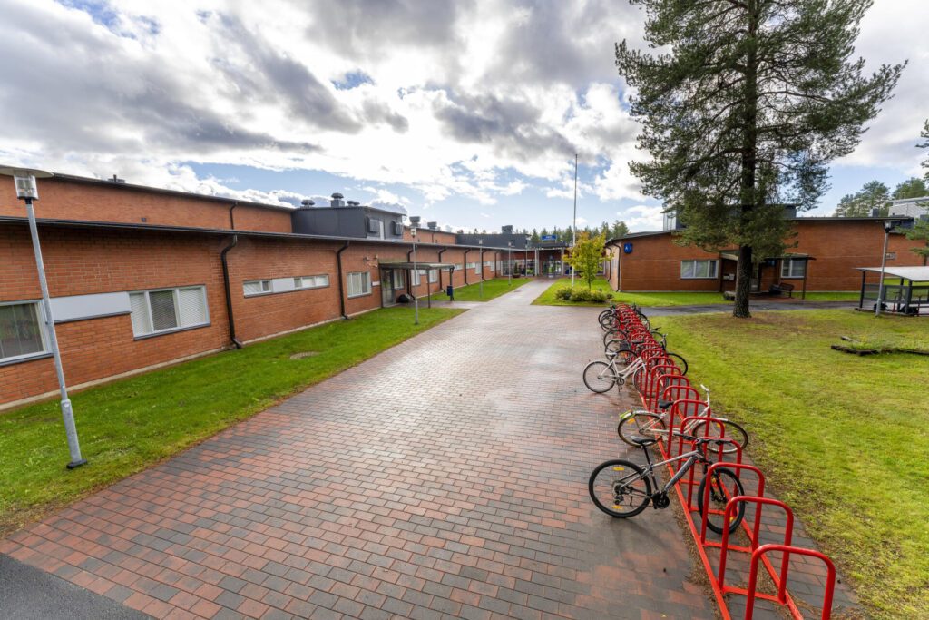 OSAOn Kempeleen toimipisteen päärakennus. Matala ja pitkä, punatiilinen rakenus. Kulkureitti laatoitettu punaisilla kivillä. Oikealla punaiset pyörätelineet ja suuri mänty.