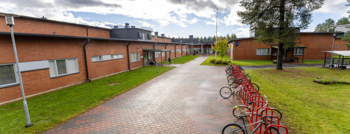 OSAOn Kempeleen toimipisteen päärakennus. Matala ja pitkä, punatiilinen rakenus. Kulkureitti laatoitettu punaisilla kivillä. Oikealla punaiset pyörätelineet ja suuri mänty.