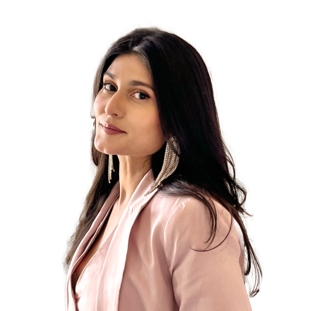 Nainen pukeutunut vaaleanpunaiseen bleiseriin, isoilla hopeisilla korvakoruilla. Hänellä on pitkät tummat hiukset ja hän hymyilee kevyesti, valkoisella taustalla.