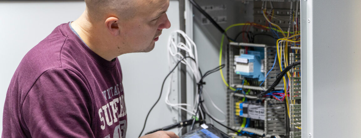 Henkilö tarkastelee avointa sähkökaappia ja käyttää tablettia.