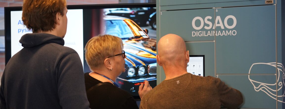 Kolme henkilöä käyttävät OSAO Digilainaamon palvelua. Taustalla näkyy auton kuva näytöllä.