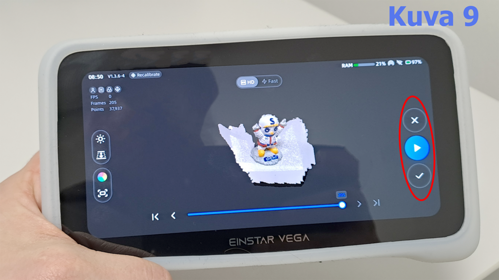 Käsi pitää kiinni EinStar Vega -laitteesta, joka näyttää 3D-mallinnusohjelman näytön. Näytöllä näkyy pienoishahmon 3D-malli. Oikealla on toimintapainikkeita, kuten X, play-kuvake ja varmistusmerkki. Yläkulmassa on tietoja, kuten aika, RAM-muistin käyttö ja akun varausprosentti. Teksti 'Kuva 9' näkyy oikeassa yläkulmassa.