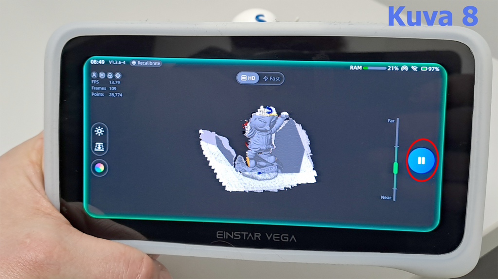 Käsi pitelee EinStar Vega -laitetta, jonka näytöllä näkyy 3D-skannaus. Näytöllä on 3D-malli hahmosta tai veistoksesta, jota skannataan. Näytöllä on myös tietoa skannausprosessista, kuten FPS, kehykset ja pisteet. Pysäytyspainike on korostettuna oikealla puolella.