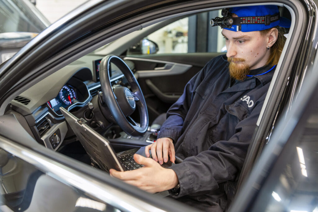 Diagnoosimekaanikko työskentelee kannettavan tietokoneen kanssa auton sisällä, päässä otsalamppu.