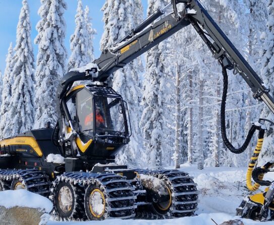 Metsäkone työskentelee lumisessa metsässä, ympärillä lumisia puita.