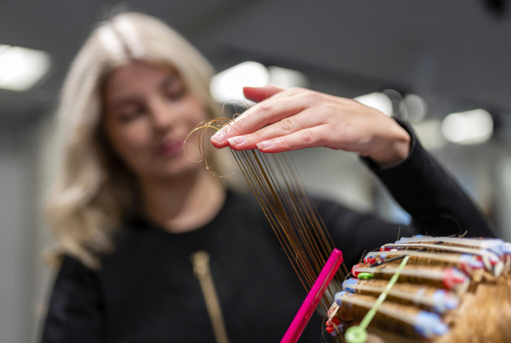 Kampaaja asettelee asiakkaan hiuksia hiustenhoitotyökalujen avulla.