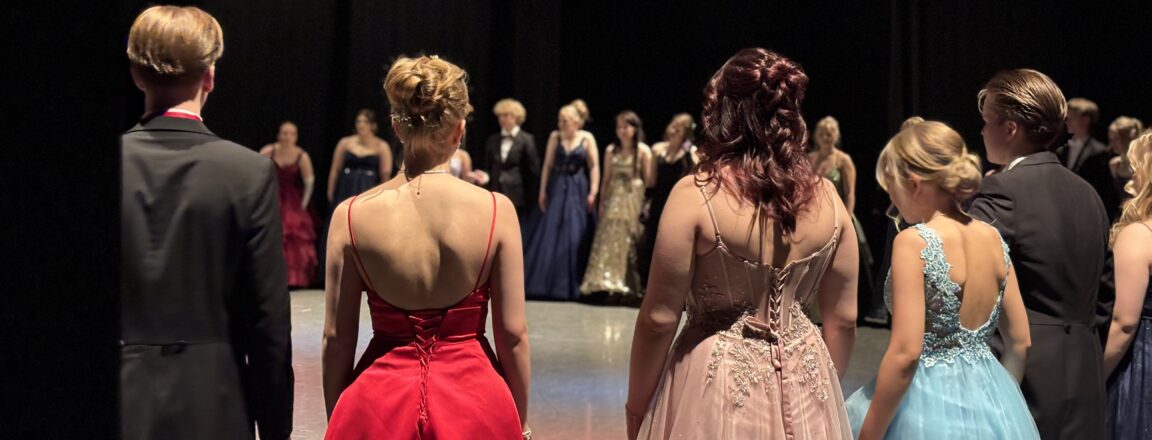 Ryhmän nuoria aikuisia juhlapuvuissa seisoo lavalla odottamassa esityksen alkua.