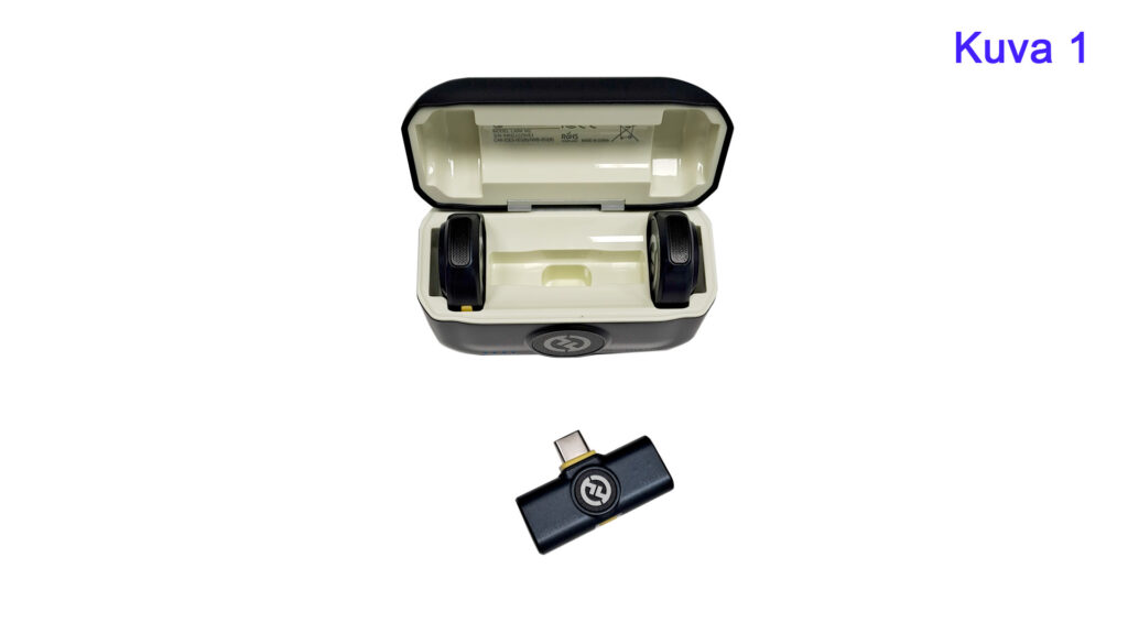Kuvassa on avattu langattoman mikrofonin kotelo, jossa on kaksi pyöreää mikrofonia ja erillinen USB-C-sovitin. Teksti 'Kuva 1' näkyy oikeassa yläkulmassa sinisellä.