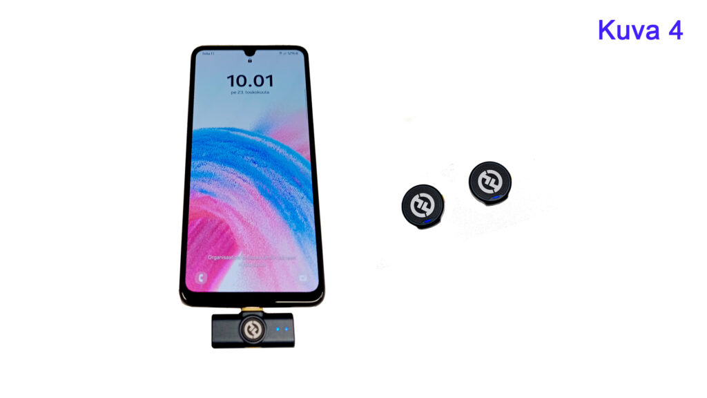 Älypuhelin, jonka näytöllä näkyy aika 10.01. Puhelimen alareunassa on langattoman mikrofonin vastaanotin kytkettynä USB-C-liittimeen. Vastaanottimessa on sininen valo. Puhelimen vieressä on kaksi pientä pyöreää langatonta mikrofonia. Ylhäällä oikealla lukee 'Kuva 4' sinisellä tekstillä.