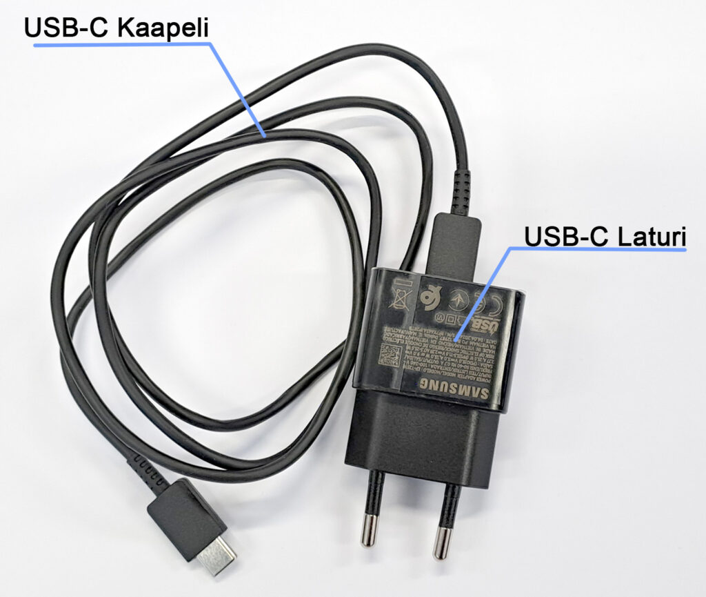 Kuvassa on Samsungin USB-C laturi ja kaapeli. Kaapeli on kiinni laturissa, ja laturissa on kaksi pistoketta. Kuvan päällä on tekstit 'USB-C Kaapeli' ja 'USB-C Laturi', jotka osoittavat kaapelin ja laturin osia.