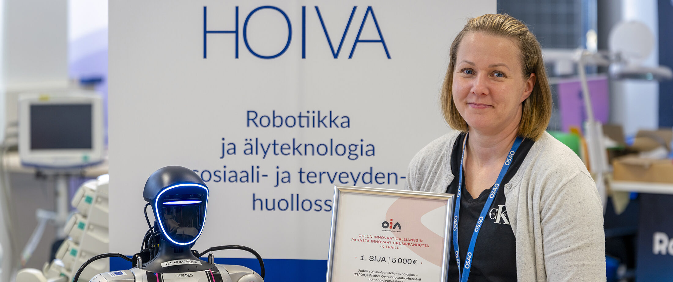 Nainen seisoo robottien vieressä pitäen sertifikaattia, jossa lukee 1. SIJA