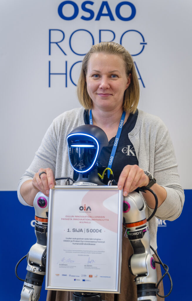 Nainen seisoo ja pitää robottia, joka pitelee palkintotodistusta.