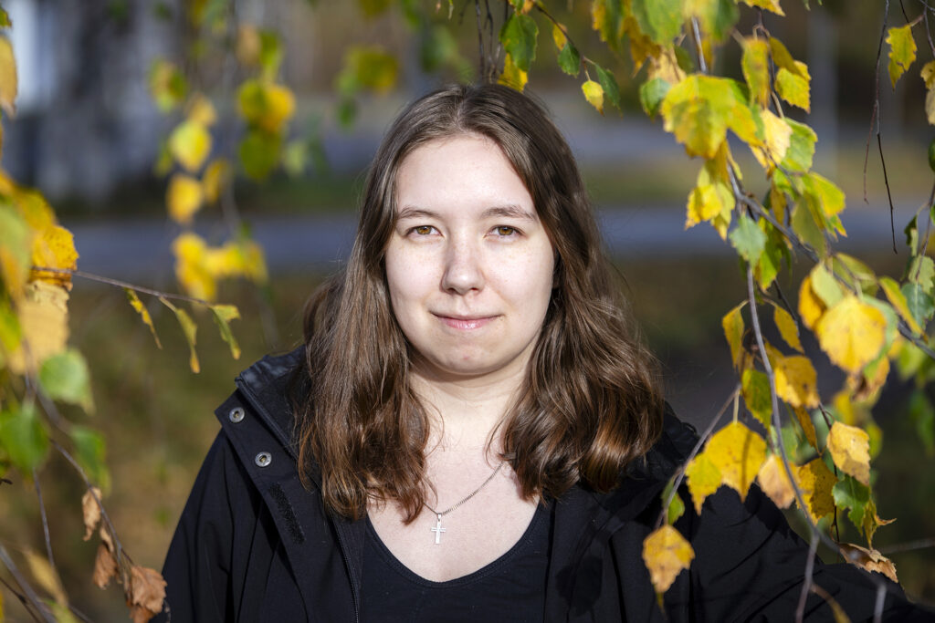 Nainen seisoo ulkona syksyisessä ympäristössä.